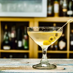 Dirty Martini on a bar top with various bottles of spirits in the background.