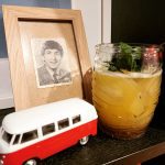 A Fog Cutter cocktail served in a Tiki glass in front of a framed picture of John Lennon.