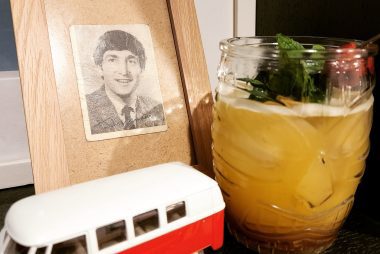 A Fog Cutter cocktail served in a Tiki glass in front of a framed picture of John Lennon.