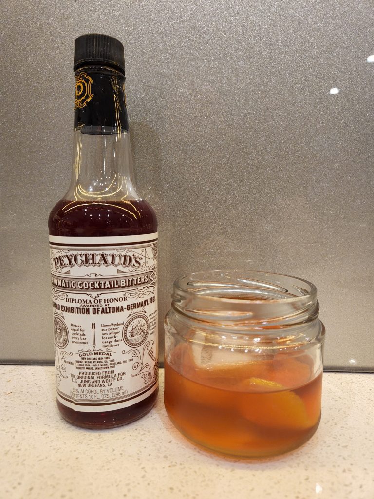An Improved Whiskey Cocktail next to a bottle of Peychaud's Bitters.