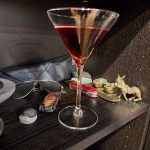 A Nutty Martini cocktail on a book shelf with assorted items behind it.