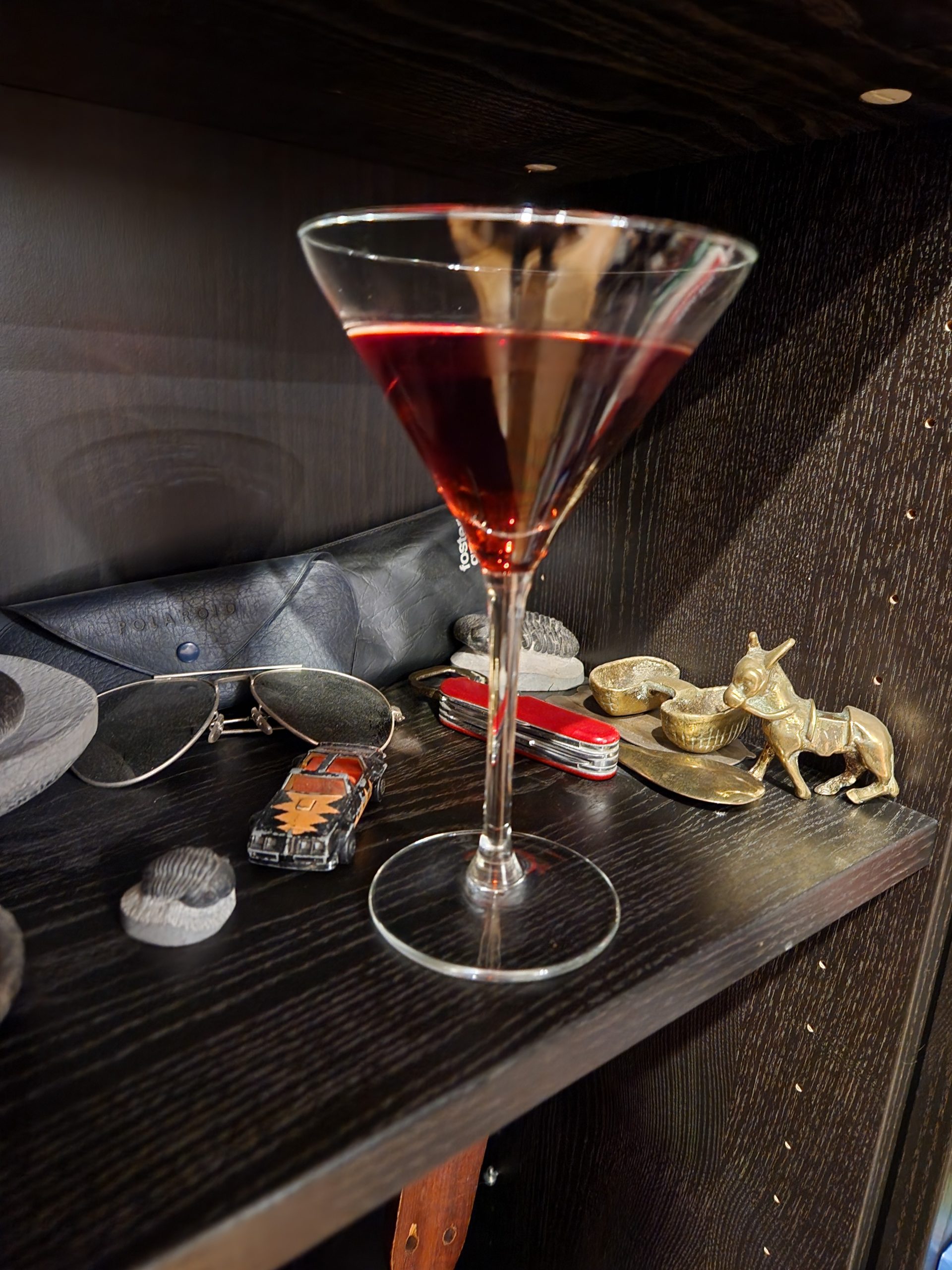 A Nutty Martini cocktail on a book shelf with assorted items behind it.