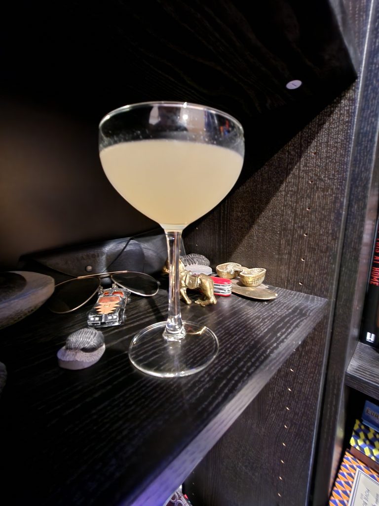 A Margarita sitting on a book shelf with assorted items.