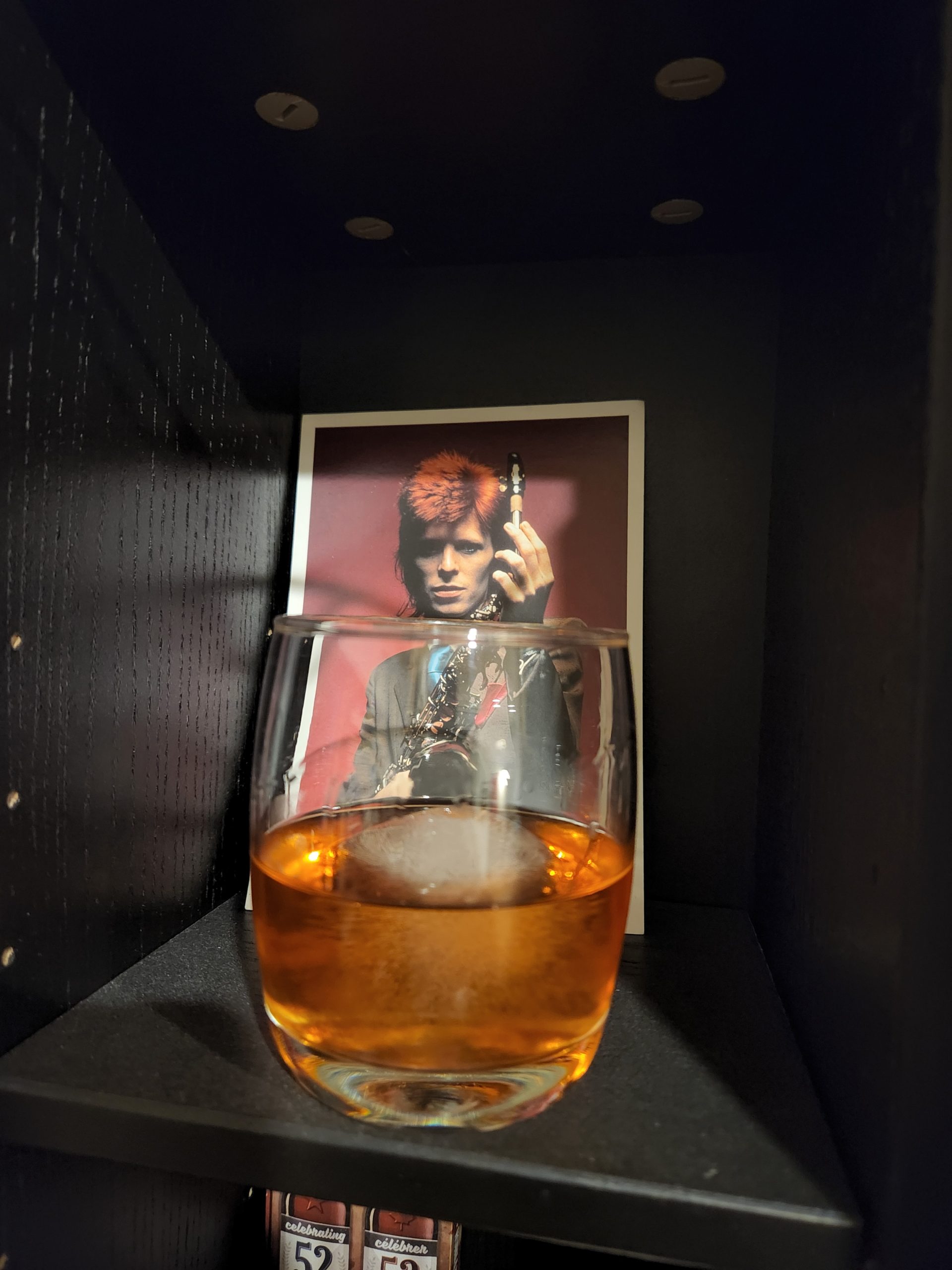 An Oaxaca Old Fashioned cocktail in front of a picture of David Bowie.