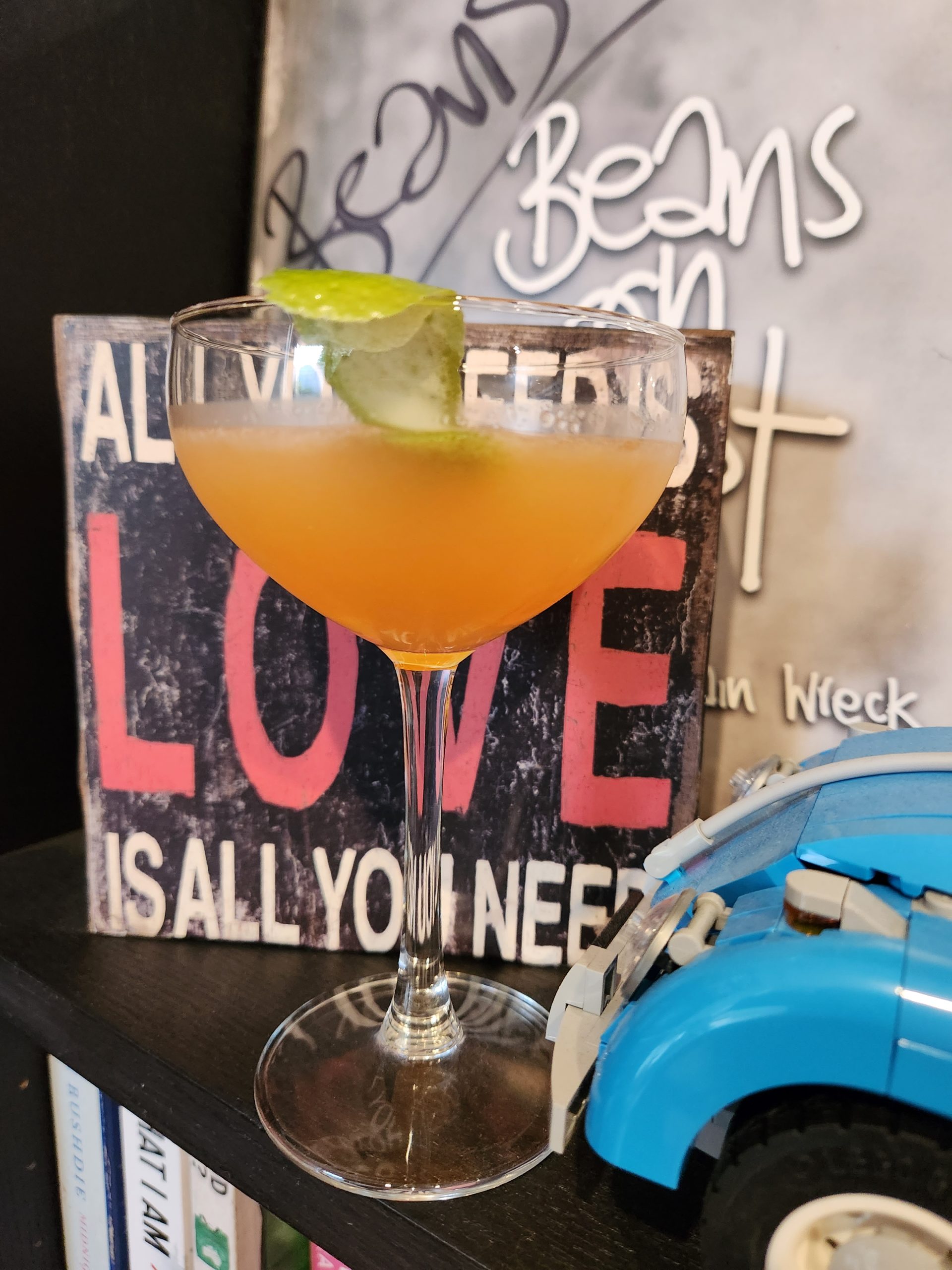 A Pegu Club Cocktail in a coupe glass sitting on a bookshelf.