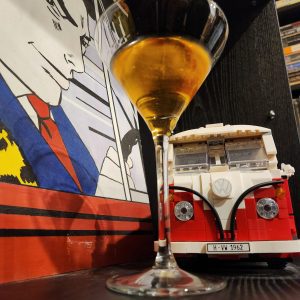 A Guadalajara Cocktail in a Martini glass on a bookcase with a Lego VW van behind it.